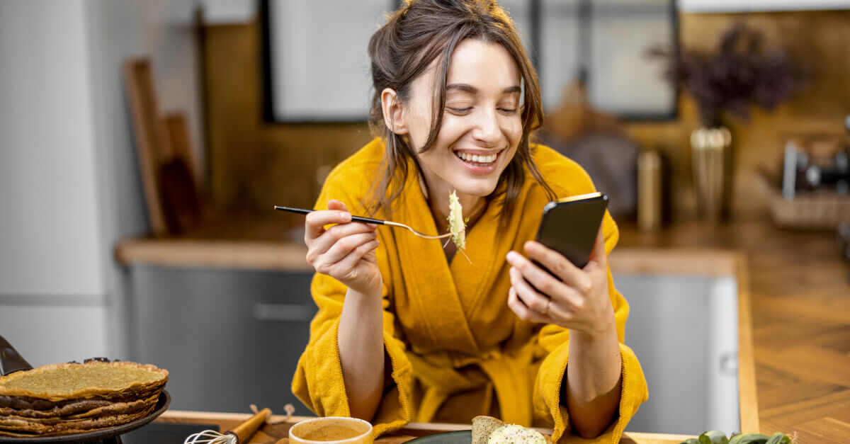 happy woman looking at her phone while eating
